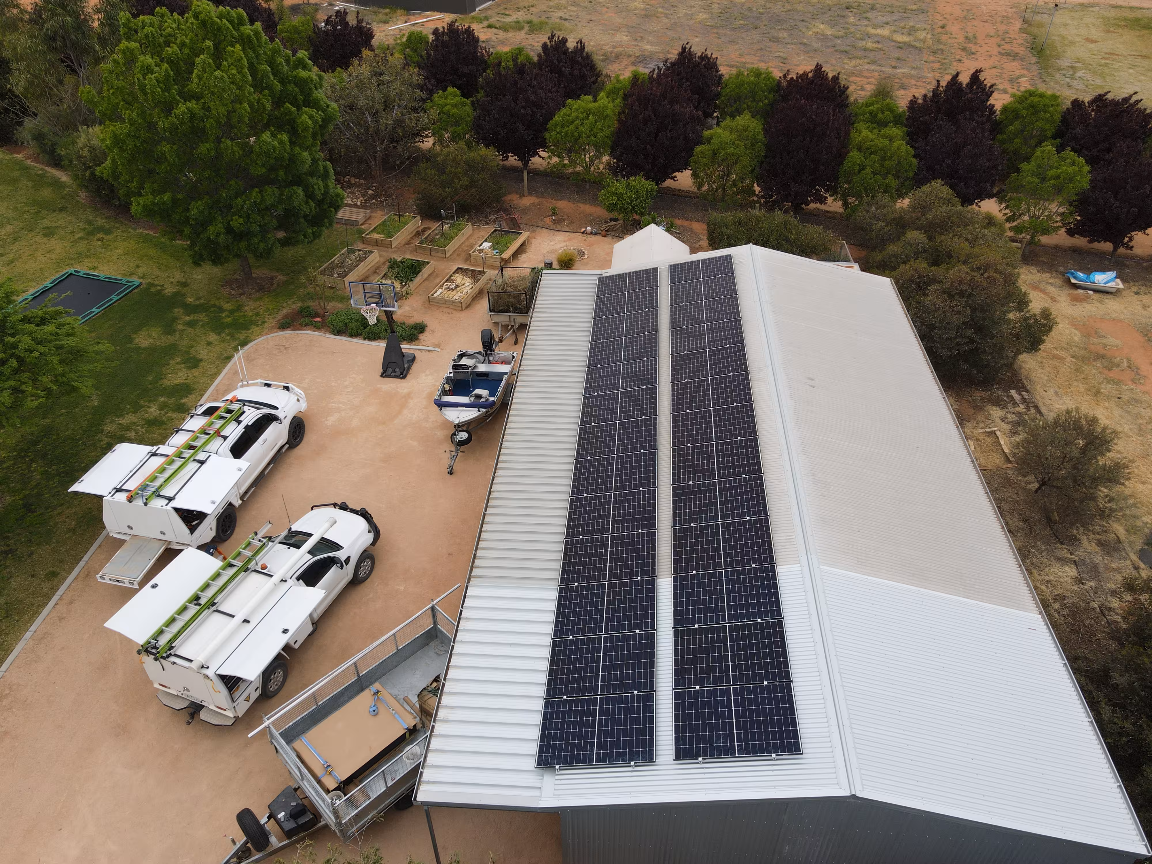 Aerial view of a RAMS residential project featuring a large shed with rooftop solar panels and two RAMS service utes on-site in a rural setting.
