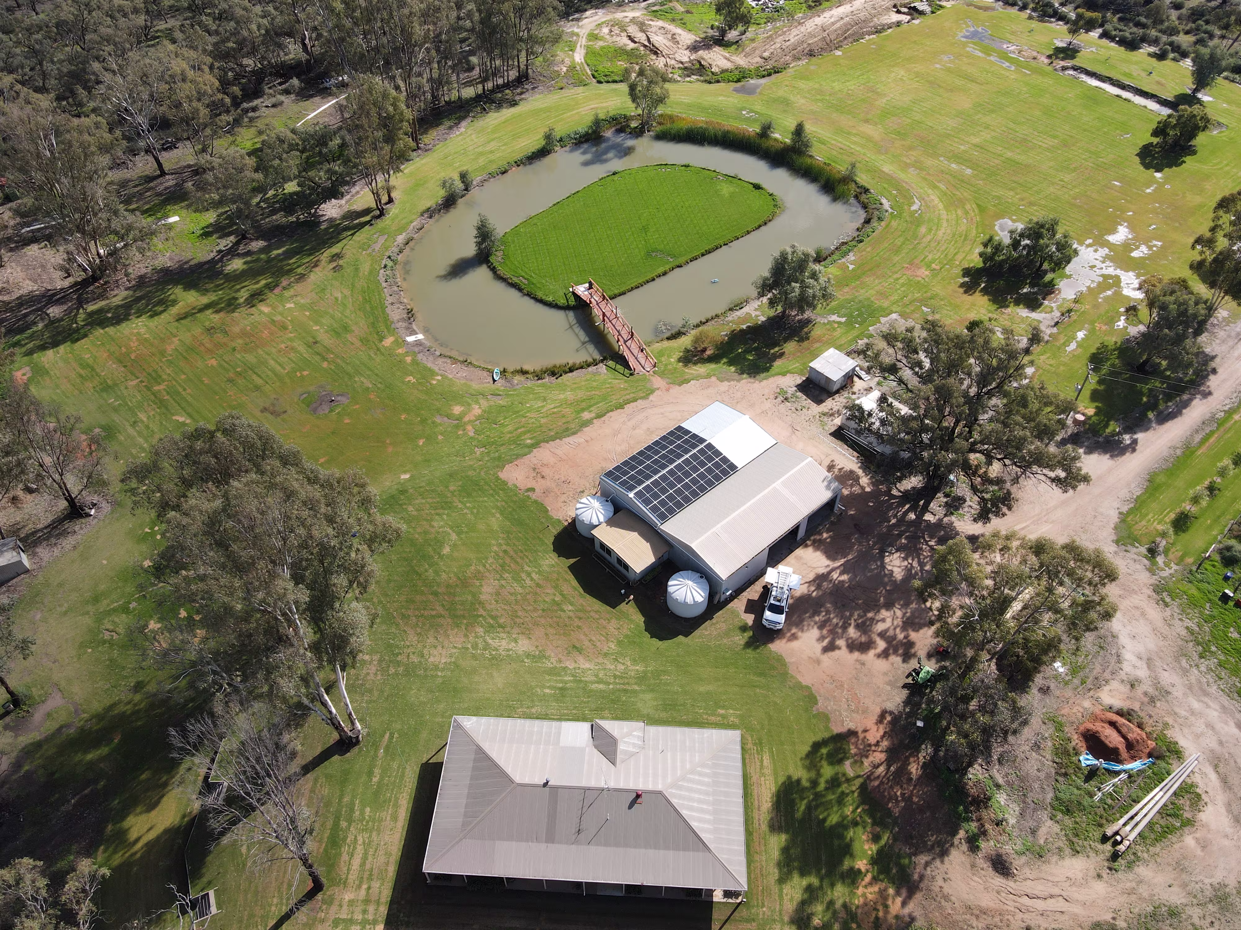 Aerial view of a large off-grid solar panel installation on a rural shed with water tanks and a service vehicle on a remote Australian station property.
