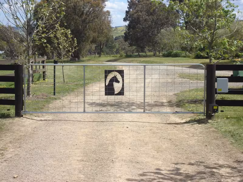 A solar-powered automatic swing gate system installed on a rural driveway entrance with a horse silhouette center panel, security control box, and heavy-duty automatic opener actuator.